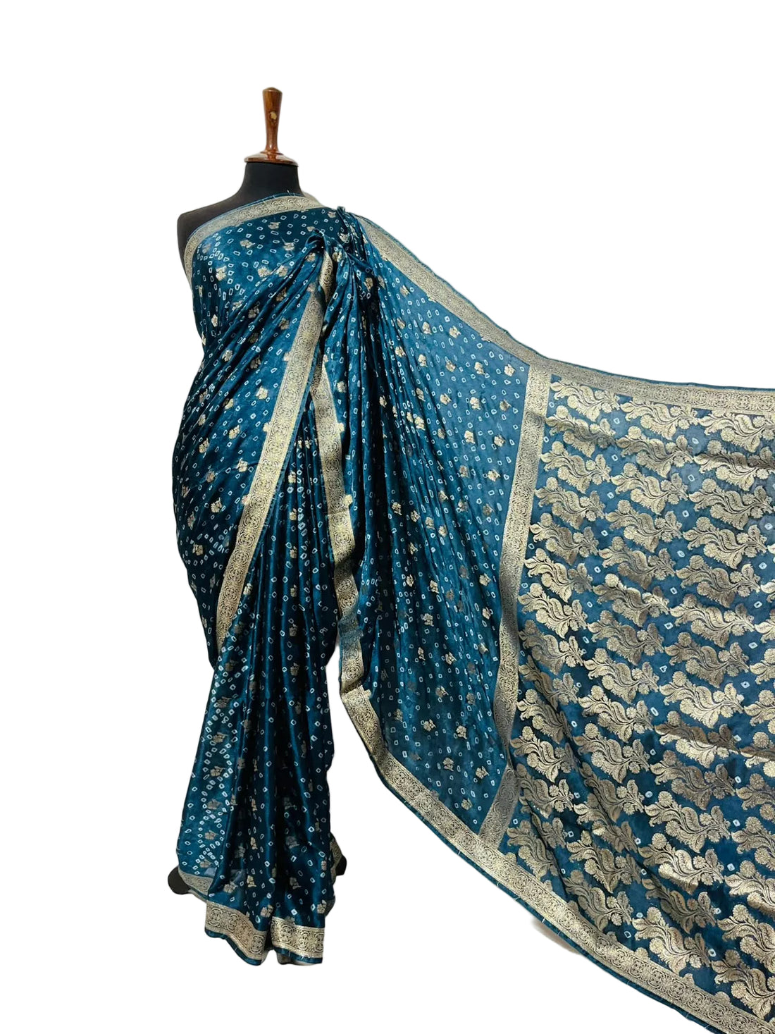 A teal blue Banarasi silk saree with gold zari floral motifs and a heavily embroidered gold border, displayed on a black mannequin torso against a white fabric backdrop.