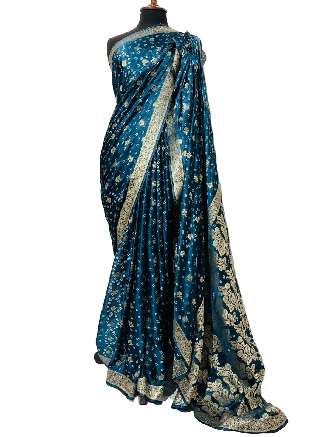 A teal blue Banarasi silk saree with gold zari floral motifs and a heavily embroidered gold border, displayed on a black mannequin torso against a white fabric backdrop.