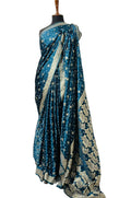 A teal blue sari with intricate silver floral motifs and a wide silver border, draped on a black mannequin torso against a white fabric backdrop.