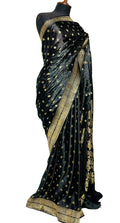 A black silk saree with gold zari motifs and a wide gold border, draped on a black mannequin torso against a white fabric backdrop.