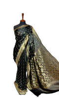 A black silk saree with gold zari motifs and a wide gold border, draped on a black mannequin torso against a white fabric backdrop.