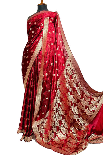 A deep red silk saree with intricate gold zari embroidery and a wide gold border, displayed on a black mannequin torso against a white fabric backdrop.