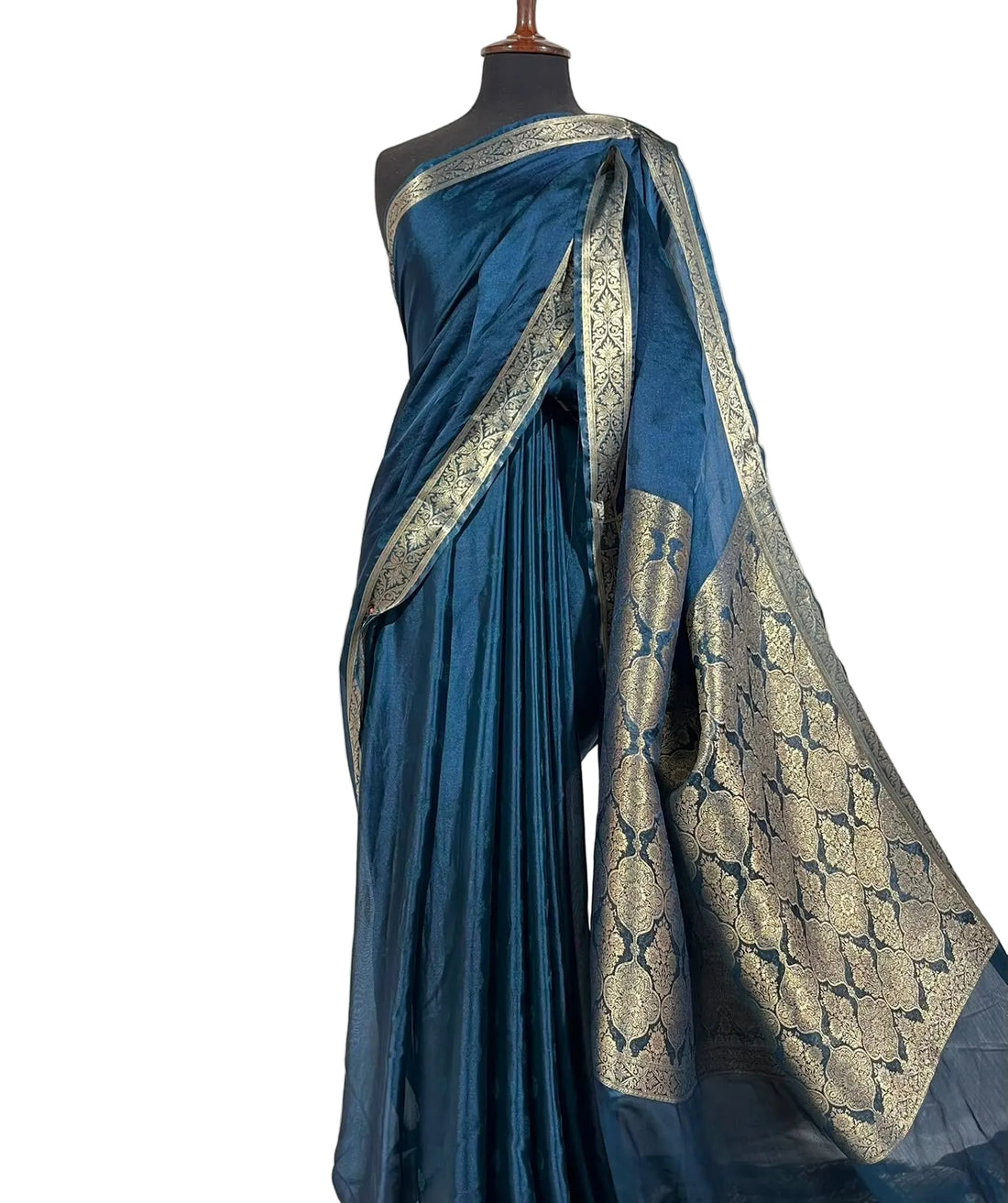 A blue silk saree with intricate gold zari brocade patterns draped on a black mannequin torso against a white fabric backdrop.