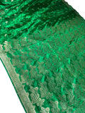 A close-up of a rich green silk saree or fabric with intricate gold zari floral embroidery and a decorative border, laid out next to a white fabric.