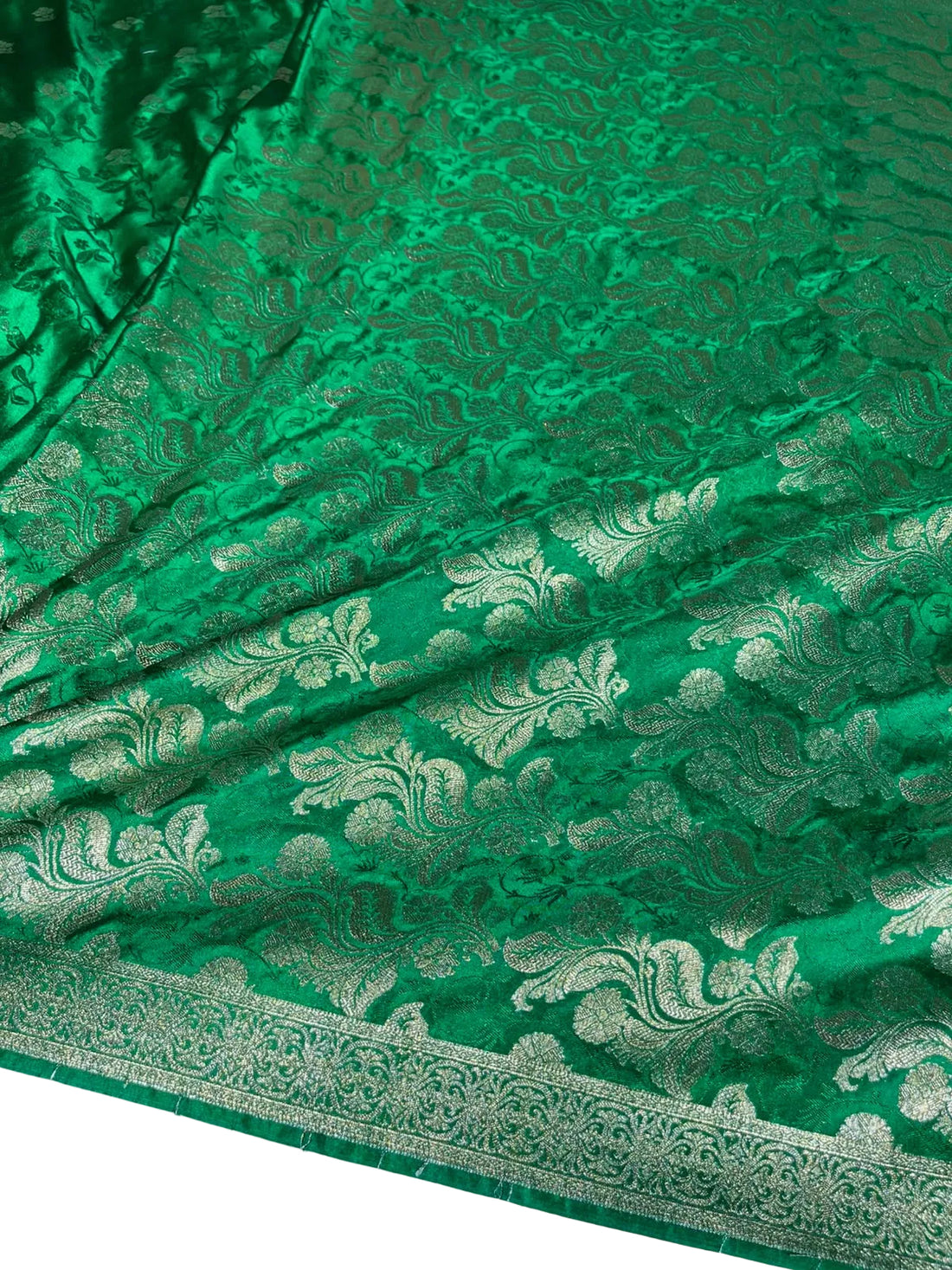 A close-up of a rich green brocade fabric with intricate metallic gold floral and paisley patterns and a decorative border.