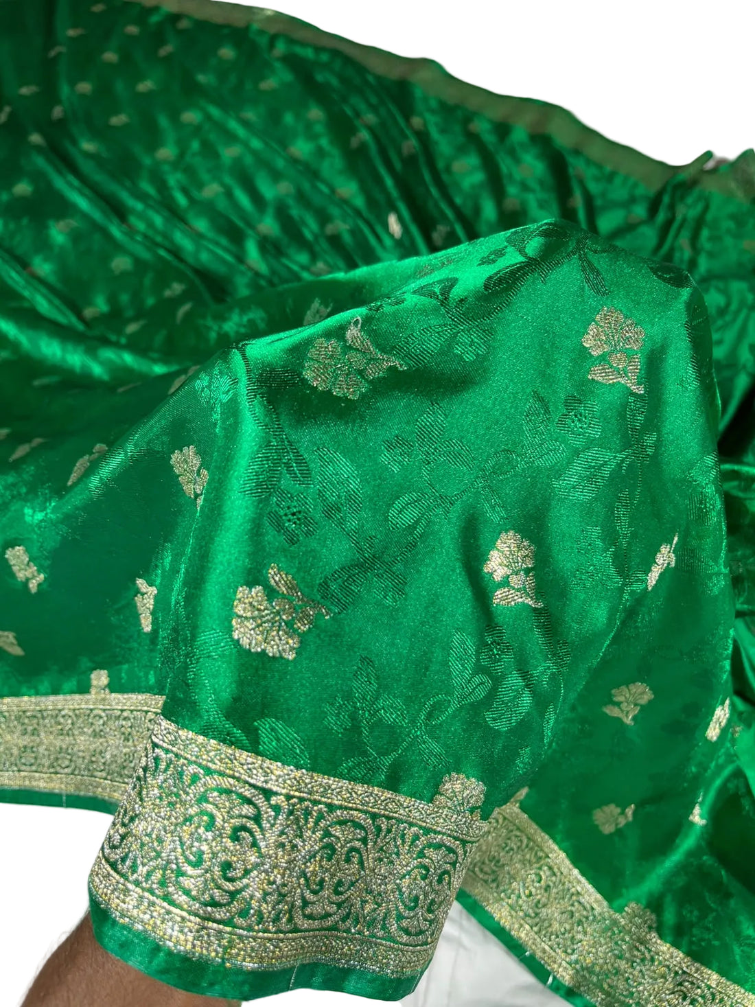 A close-up of a rich green brocade fabric with intricate metallic gold floral and paisley patterns and a decorative border.
