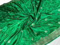 A vibrant green silk saree or fabric draped in a swirl, featuring metallic gold floral motifs and a decorative gold border along the edge.