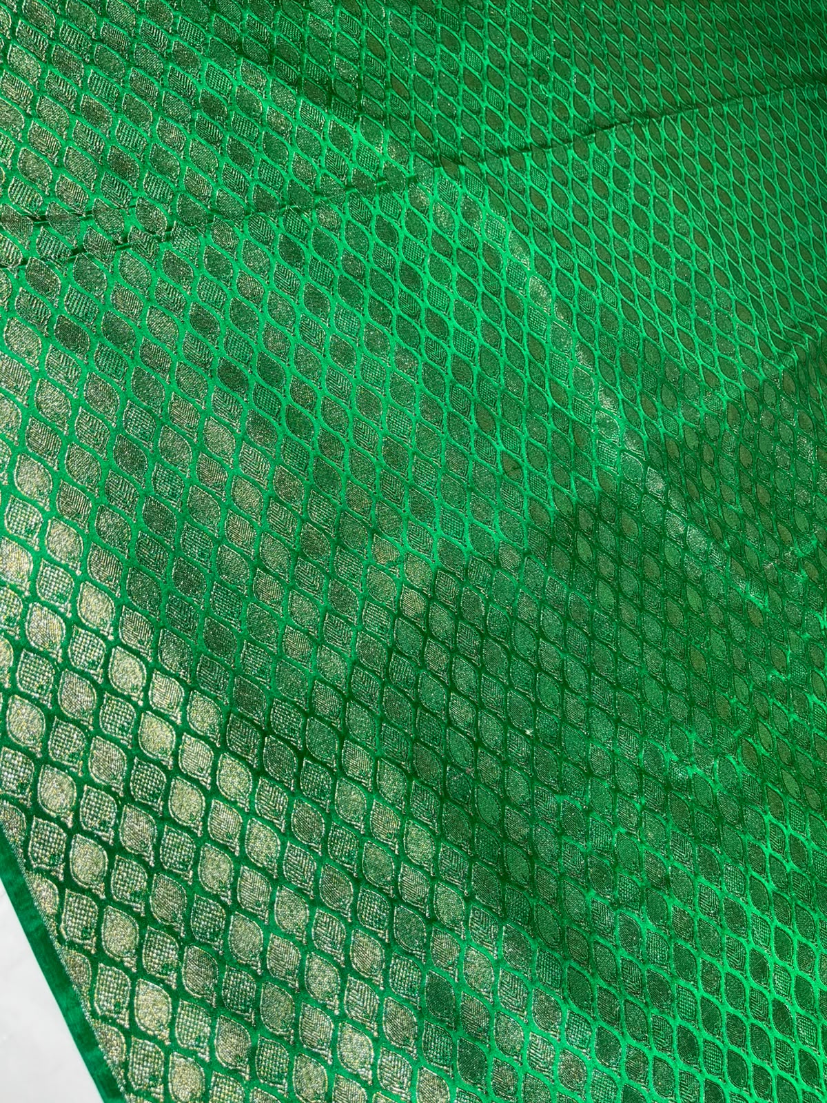 A close-up of bright green mesh fabric or netting with a diamond-pattern grid, draped with visible folds and texture.